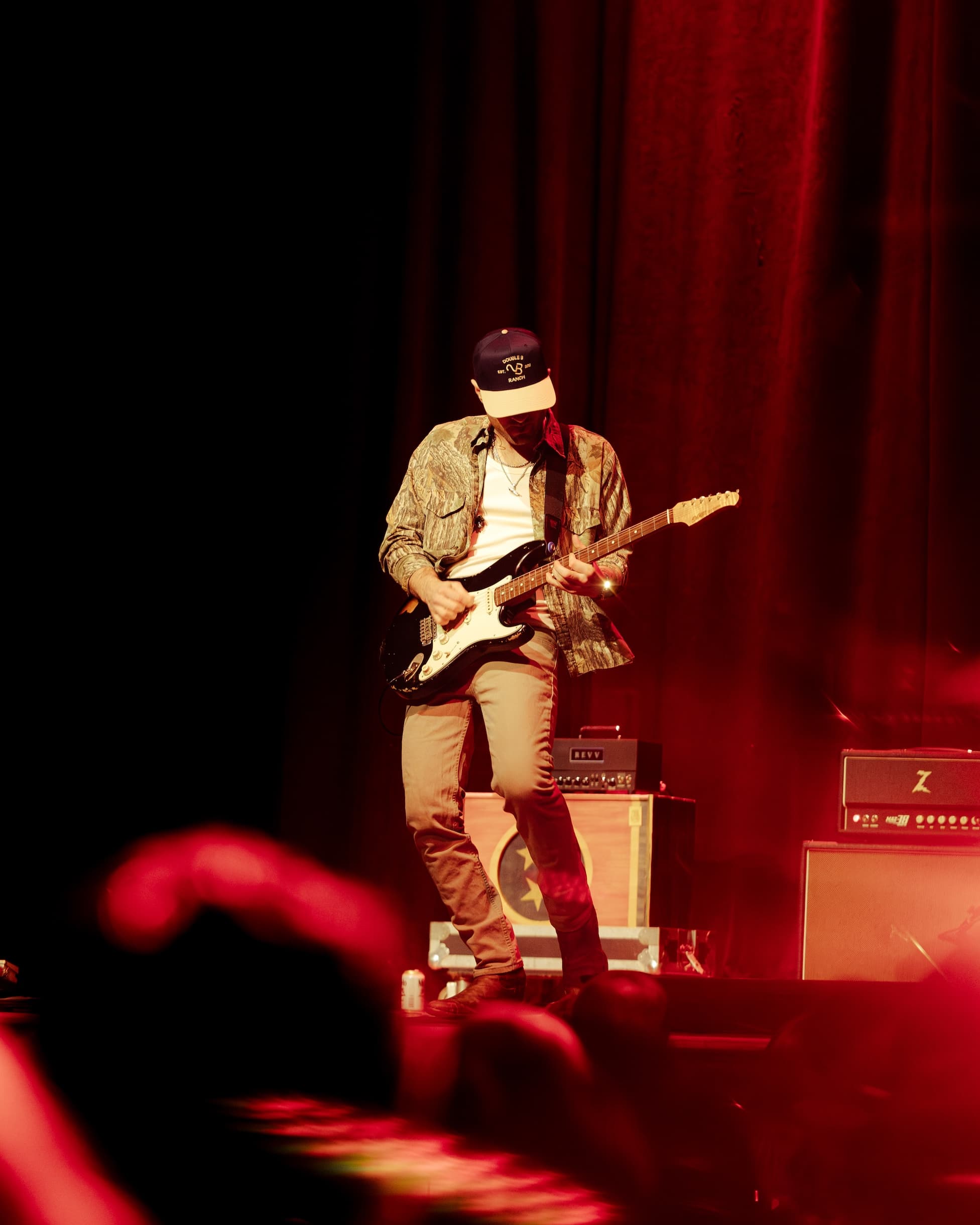 Greylan James playing guitar on stage under red lights
